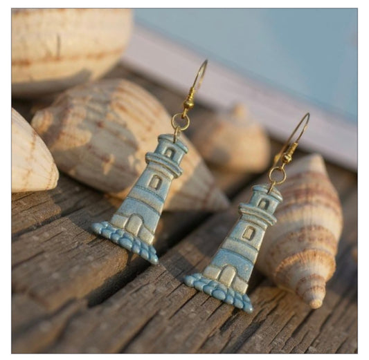 Lighthouse-shaped earrings on a wooden surface with seashells