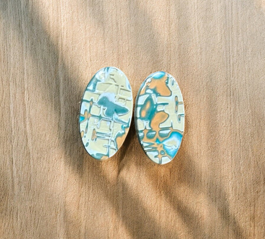 Oval-shaped earrings mokume gane with a geometric pattern on a wooden surface