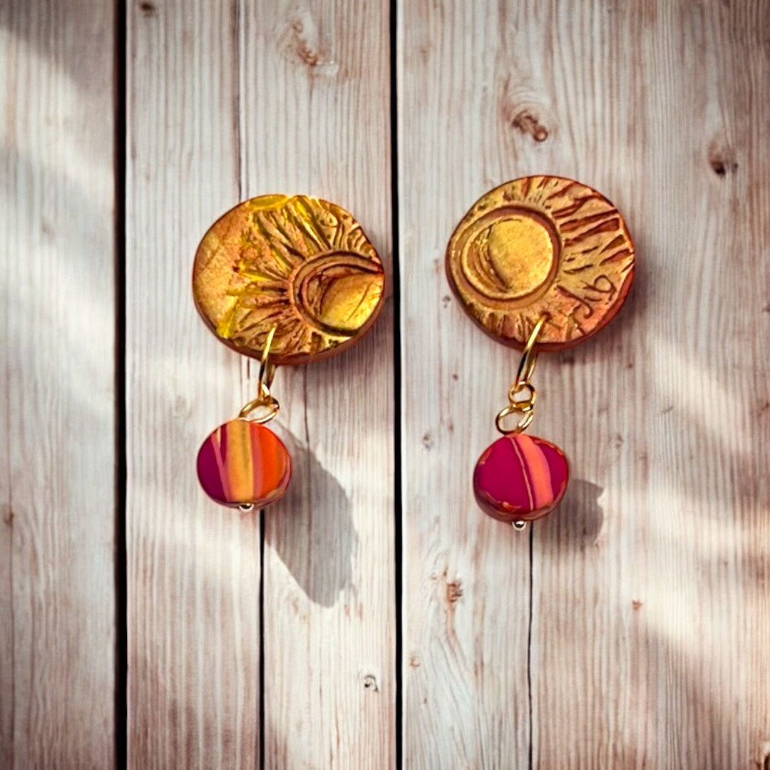 Pair of gold and red sunburst design earrings on a wooden surface