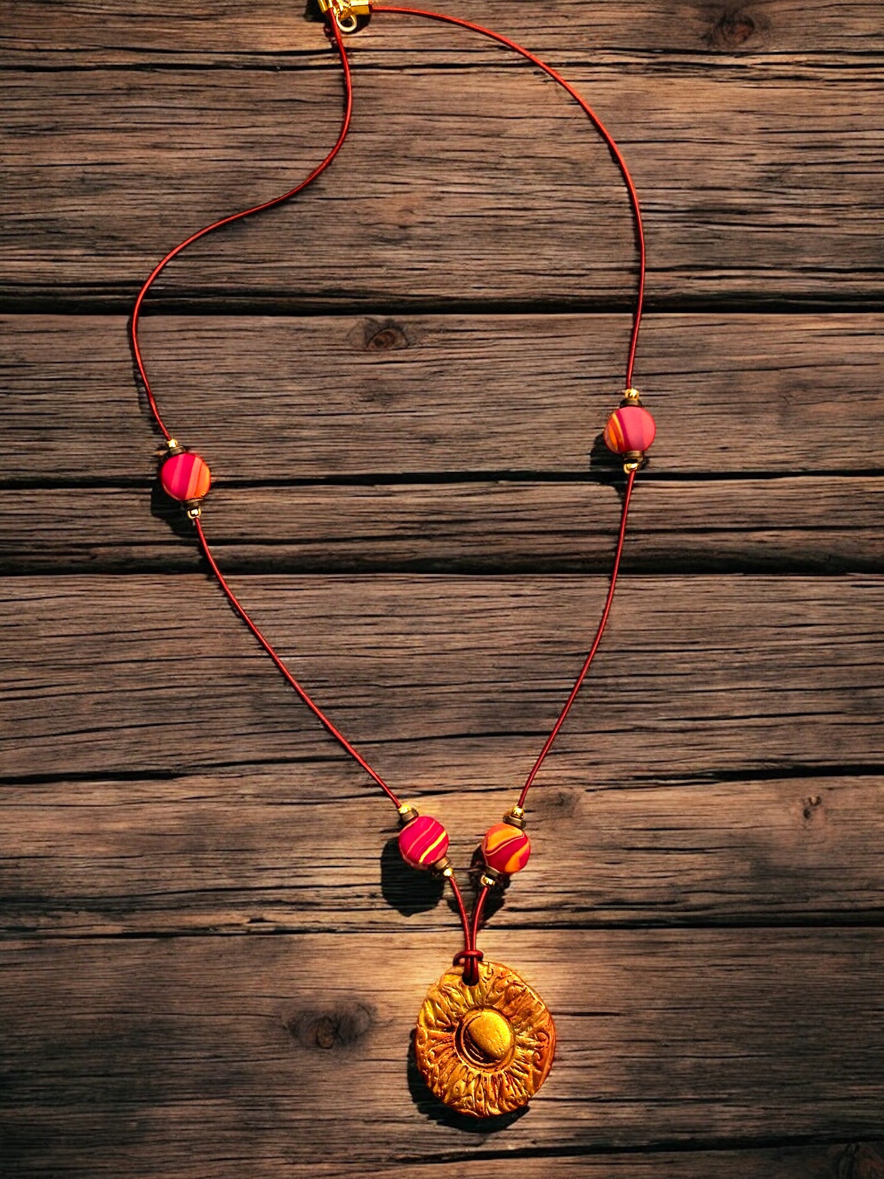 Sunburst Necklace with red cord and colorful beads on a wooden surface