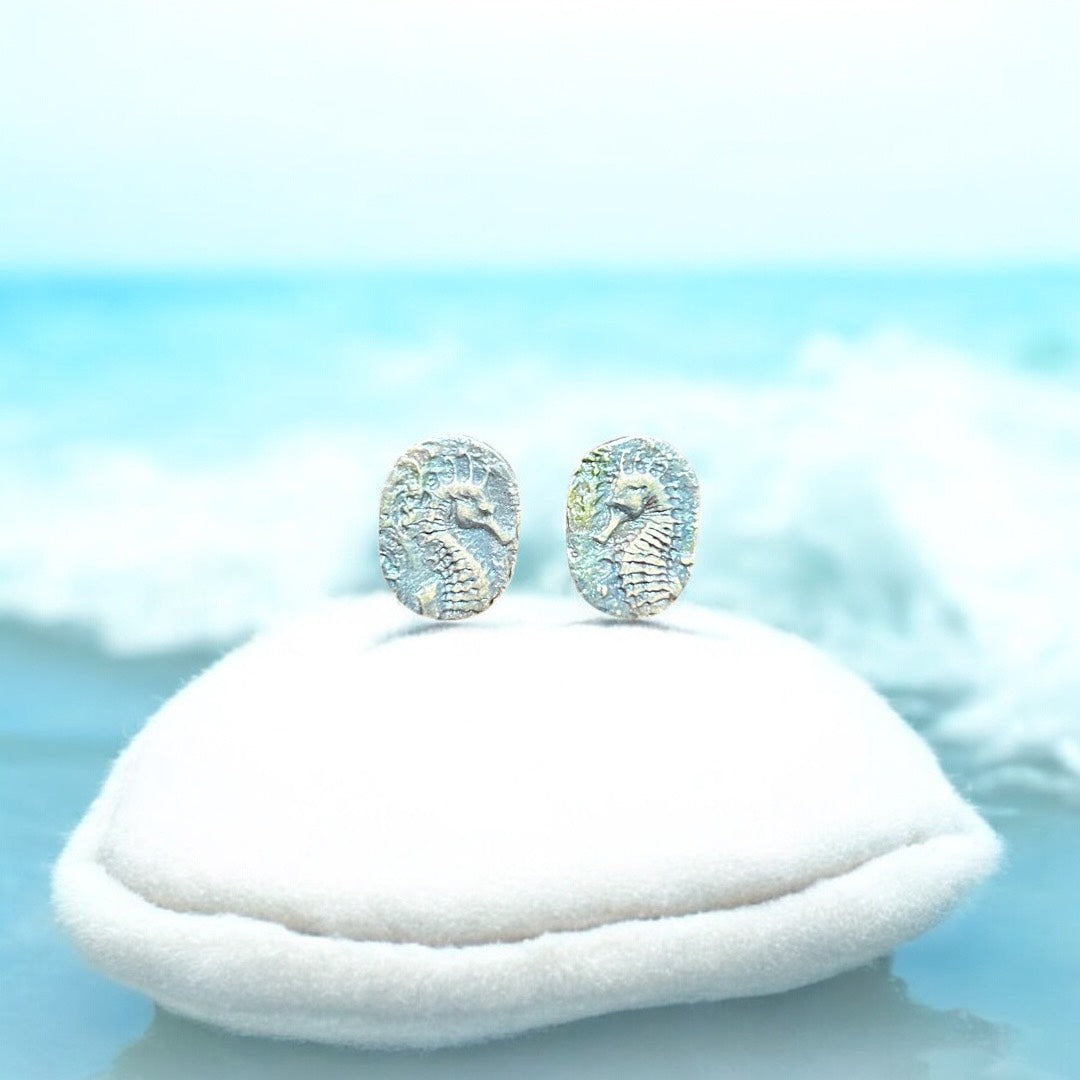 Pair of seahorse earrings on a white cushion with a light blue background