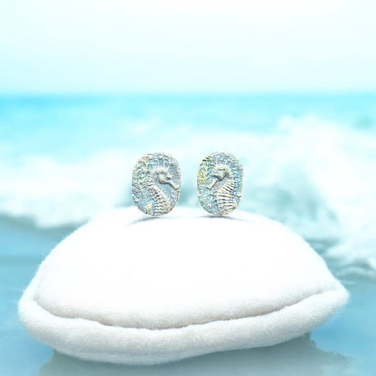 Pair of seahorse earrings on a white cushion with a light blue background